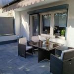 Terrasse mit Sitzgruppe, Tisch und Sonnenschutz. Fenster mit Pflanzen.