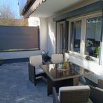 Terrasse mit Sitzgruppe, Sonnenschutz und Pflanzen. Glas-Tisch und Fenster zur Wohnung.