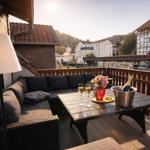 Terrasse mit Sitzgruppe, Tisch, Champagner und Blumen. Blick auf Fachwerkhäuser und Hügel.