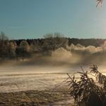 Frostbedeckte Bäume und ein nebliger See bei Sonnenaufgang.