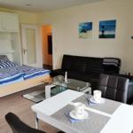 Ein Schlafzimmer mit Bett und Schränken. Wohnbereich mit Sofa, Tisch und Stühlen. Wandbilder mit Leuchtturm.