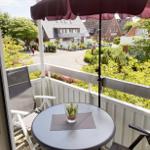 Balkon mit Tisch, Stühlen und Sonnenschirm. Blick auf grüne Umgebung und Straße.