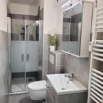 Badezimmer mit Dusche, Waschbecken und Toilette. Graue Fliesen und Spiegelschrank.