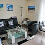 Wohnzimmer mit Sofa, Sessel und Glas-Tisch. Wandbilder zeigen Strand und Leuchtturm.