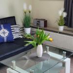 Schwarzes Sofa mit Kissen, Glas-Tisch und Blumen. Wandbild zeigt Strand.