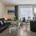 Wohn- und Essbereich mit Sofa, Tisch und Stühlen. Fenster mit Vorhängen und Wandbild.