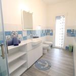 Badezimmer mit Dusche, Waschbecken und Toilette. Blaue Fliesen und grauer Boden.