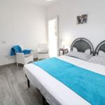 Schlafzimmer mit Doppelbett, zwei Stühlen und Tür zum Balkon.