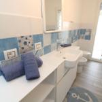 Badezimmer mit blau-weißen Fliesen, Waschbecken, Toilette und Badematte mit Ankern.