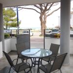 Terrasse mit Tisch und Stühlen, Blick auf Straße und Meer.