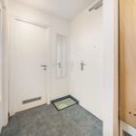 Eingangsbereich mit Tür, Spiegel und Fußmatte auf Fliesenboden.