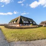 Haus mit Grashütten-Dach auf grünem Grundstück unter blauem Himmel.