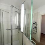 Duschkabine mit Glaswand und Handbrause, daneben Handtuchhalter mit Handtüchern.