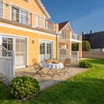 Haus mit Terrasse, Tisch und Stühlen im Garten. Weiße Gittertore und grünes Gras.