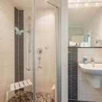 Dusche mit Sitzbank, Waschbecken und Spiegel