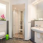 Badezimmer mit Dusche, Waschbecken und Toilette. Pinker Blumenstrauß auf Regal.