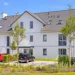 Modernes weißes Mehrfamilienhaus mit Dachfenstern und Parkplatz.