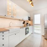 Küche mit weißen Schränken, Edelstahl-Kühlschrank und Fenster zur Außenseite.
