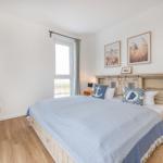 Schlafzimmer mit Bett, Fenster und Wandbildern.