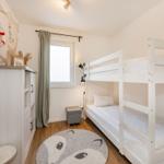 Ein Schlafzimmer mit Doppelstockbett, Fenster, Gardine und dekorativen Wandelementen.