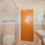 Badezimmer mit Dusche, Waschbecken und Holztür.