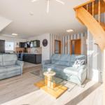 Wohn- und Küchenbereich mit zwei Sofas, Glas-Tisch und Holztreppe.