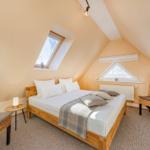 Schlafzimmer mit Dachschrägen, Bett, zwei Stühlen und zwei Fenstern.
