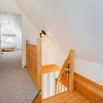 Treppenhaus mit Holzgeländer führt zu einem Schlafzimmer mit Dachfenster.