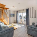 Wohnzimmer mit zwei Sofas, Glas-Tisch und Holztreppe. Balkon mit Blick nach draußen.