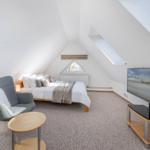 Schlafzimmer mit Dachschrägen, Bett, Sessel und Fernseher.