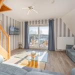 Wohnzimmer mit Sofa, Glas-Tisch und Balkonansicht. Holztreppe und gestreifte Wände.