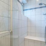 Duschkabine mit Sitzbank, Duschbrause und Heizkörper an der Wand.