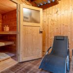 Sauna mit Holzbanken und zwei Liegestühlen vor der Tür.