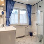 Badezimmer mit Dusche, Waschbecken und Fenster mit Vorhängen.