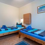 Zwei Betten mit blauen Bettwäschen, Wand-TV und Holzmöbel.