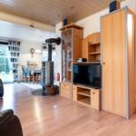 Wohnzimmer mit Holzboden, Sofa, TV und Kaminofen. Essbereich mit Tisch und Stühlen.