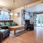 Wohnzimmer mit Ledersofa, Holztisch und Fenstern mit Gardinen.