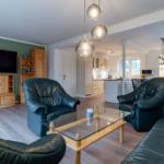 Wohnzimmer mit Ledersofa, Glas-Tisch und Fernseher. Küche im Hintergrund.