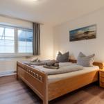 Schlafzimmer mit Holzbett, Nachttisch und Fenster mit Vorhängen.