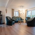 Wohnzimmer mit Ledersofa, Sesseln, Holzboden und Fenstern.