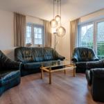 Wohnzimmer mit schwarzen Ledermöbeln, Glas-Tisch und großen Fenstern.