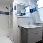 Badezimmer mit Dusche, Waschbecken und Spiegel unter Dach