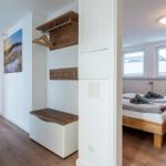Schlafzimmer mit Bett und Fenstern. Flur mit Kleiderständer und Bild.