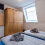 Zimmer mit zwei Betten, Kleiderschrank und Dachfenster. TV und Spielplatte an der Wand.