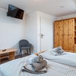 Zimmer mit Doppelbett, Holzschrank und Wand-TV.