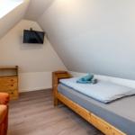Zimmer mit Dachschrägen, Bett, Kleiderschrank und Wand-TV.
