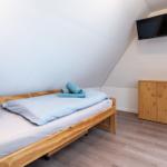 Schlafzimmer mit Bett, Kleiderschrank und Fernseher an der Wand.