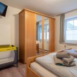 Zimmer mit Bett, Kleiderschrank und Babybett. Fenster mit Jalousien und Wand-TV.