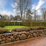 Haus mit Steinmauer, Rasen und Hecken im Garten