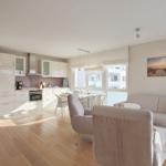 Wohn- und Essbereich mit Küche und großem Fenster. Sofa, Sessel und Tisch sind vorhanden.